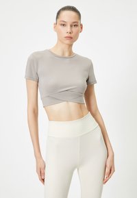 T-shirt cropped grigio chiaro con maniche corte e dettaglio frontale attorcigliato, abbinato a leggings crema a vita alta realizzati in un tessuto morbido e elastico.