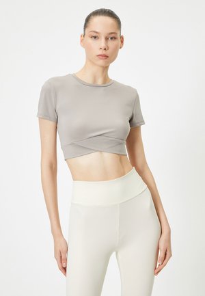 Lichtgrijs cropped t-shirt met korte mouwen en een gedraaide voorkant, gecombineerd met hoogstaande crème legging in een gladde, rekbare stof.