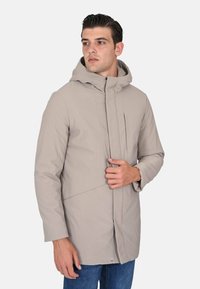 Giacca beige chiaro con cappuccio, taglio dritto, chiusura con zip e dettagli con tasca frontale. Texture morbida e design minimalista.