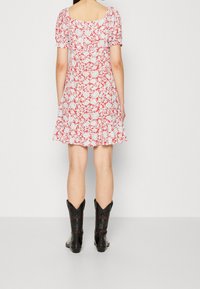 Červené a bílé květinové šaty s krátkými nafouklými rukávy, čtveratým výstřihem a splývavou sukní, doplněné černými kovbojskými botami s ozdobnými detaily.