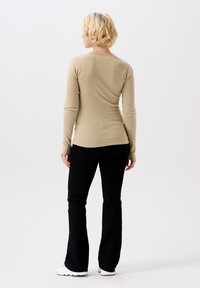Beige Langarmshirt mit weitem Ausschnitt, kombiniert mit schwarzen Schlaghosen und weißen Sneakers, von hinten vor einem hellen Hintergrund betrachtet.