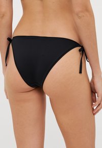 Black bikini bottom featuring tie-side closures, a smooth texture, and a classic design with minimal coverage and curved back.