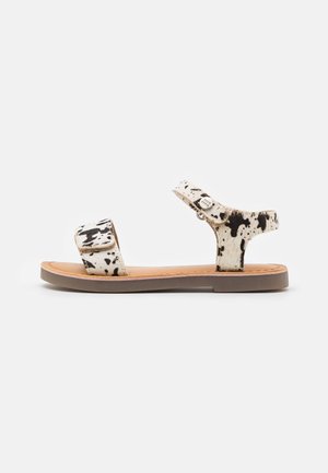 Zapatos de sandalias de cuero de vaca con un patrón blanco y negro con manchas, suela plana, correa ajustable y un diseño simple.