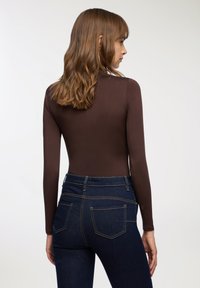 Body in tessuto marrone a maniche lunghe abbinato a jeans a vita alta blu scuro. Tessuto liscio, design aderente, cuciture evidenti sulle tasche.