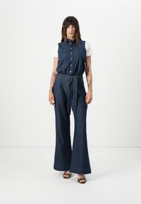 Denim overall met een aansluitend lijfje en wijde pijpen, voorzien van een knoopsluiting aan de voorkant, kraag en een strik in de taille. Donkerblauwe kleur en een zachte textuur.