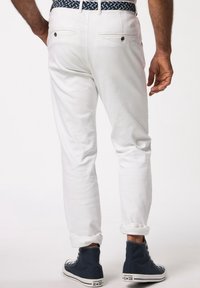 Pantaloni bianchi in cotone a taglio slim, con tasche posteriori e risvolti, abbinati a sneakers alte blu navy. Accentuati da una cintura intrecciata.
