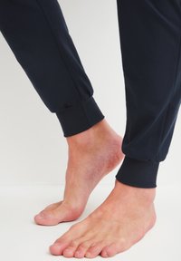 Marinefarbene Jogginghosen aus weichem Stoff, mit elastischen Bündchen an den Knöcheln. Nackte Füße sind in der Nähe des Saums sichtbar.