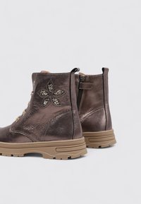 Bottines métalliques marron avec des accents floraux décoratifs, fermeture éclair latérale et semelle en caoutchouc durable. Finition en cuir texturé.