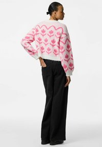 Maglione a maglia corto con motivo floreale rosa su sfondo bianco. Jeans neri a gamba larga, texture liscia e vestibilità rilassata.