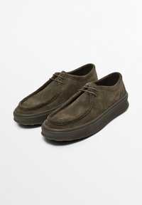 Chaussures brunes en suede à enfiler avec un bout rond, un laçage minimal et une semelle en caoutchouc texturée. Présente une plateforme légèrement surélevée.