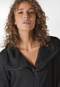 Sudadera negra con cremallera y un gran cuello drapeado. Fabricada con tela texturizada, presenta un cuello alto y un brillo sutil.