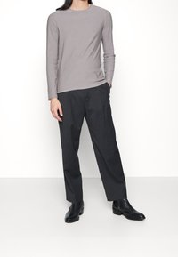 Szara koszula z długim rękawem o szczupłym kroju, zestawiona z ciemnoszarymi spodniami i czarnymi botkami, stojąca na białym tle.