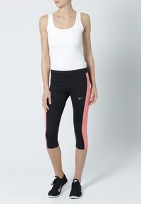 Black athletic capris with pink side accents and a fitted design. Paired with a white sleeveless top and black sneakers.