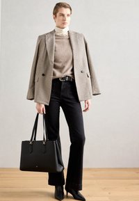 Blazer a scacchi sopra un maglione beige, jeans neri con orli svasati e scarpe nere con tacco alto. Borsa nera strutturata, texture liscia.