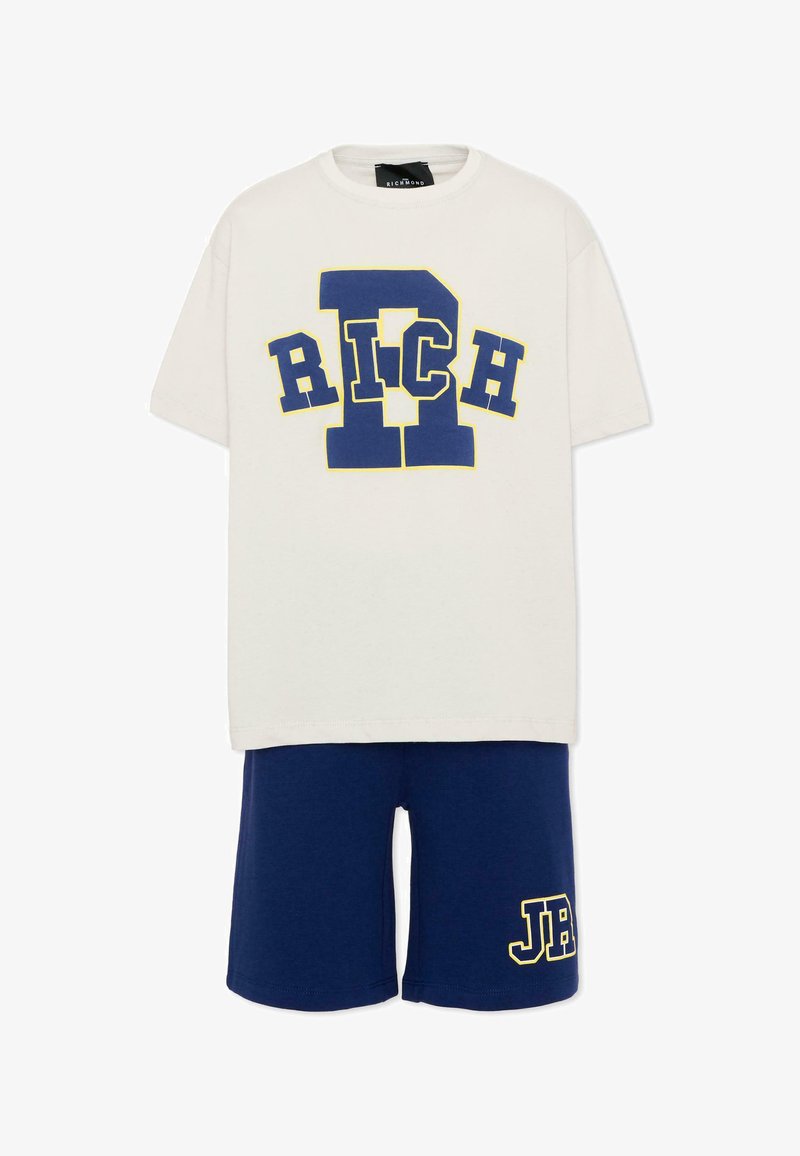T-shirt blanc à manches courtes avec un grand texte bleu "RICH" et un short bleu marine comportant des lettres "JB" soulignées de jaune sur la jambe gauche.