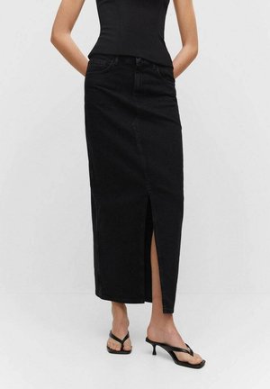 Gonna lunga in denim nero con spacco frontale, aderente in vita e taglio dritto. Abbinata a sandali neri con tacco e cinturini.