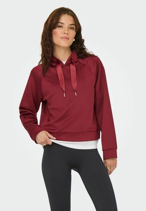 Bordeaux hættebluse med en kort design, satin snore og ribbede manchetter, kombineret med sorte leggings. Glat stofstruktur.