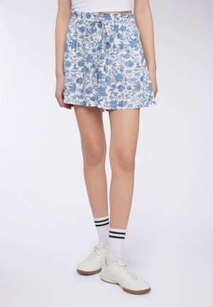 Skort con stampa floreale in bianco e blu, vita elasticizzata con cordoncino, silhouette svasata, indossato con sneaker bianche e calzini a righe.