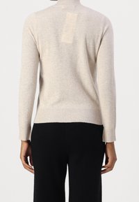 Beige stickad tröja med långa ärmar, hög krage, ribbade muddar och fåll, samt en rektangulär detalj på baksidan. Mjukt, texturerat tyg.