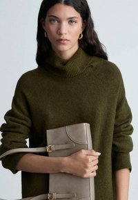 Maglione verde oliva a maglia grossa con colletto alto, abbinato a una pochette grigia chiaro con dettagli color beige e fibbia.