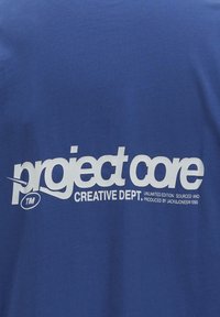 Camiseta de algodón azul con una gran impresión blanca que dice "project core" y "Creative Dept." Textura suave, diseño de cuello redondo.