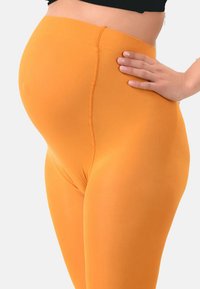 Leggings arancioni brillanti con una texture liscia e stretchy. Vita alta e design aderente, che enfatizza una silhouette tondeggiante.