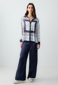Chemisier à manches longues et boutonnage avec un motif cachemire blanc et marine et un col contrastant, associé à un pantalon large marine et des baskets blanches.