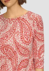 Roze geblokte blouse met een ronde halslijn en driekwartmouwen. Het ontwerp bevat onregelmatige vlekken in tinten van rood en wit.