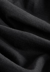 Črna tkanina z mehko, teksturirano površino, prikazani so padajoči gubasti gubi in fin vzorec tkanja. Brez vidnih vzorcev ali okraskov.