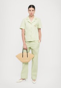 Light green short-sleeve shirt with buttons and embroidered detail, paired with matching trousers. Accessorized with a round straw bag.