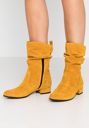 Gele suède enkellaarzen met een slouchy ontwerp, zijrits, lage blokhak en een gladde textuur, met een ronde neus en gestikte accenten.