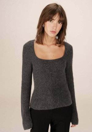 Pull gris texturé avec un décolleté carré et des manches longues, fabriqué à partir d'un matériau doux et duveteux. Design ajusté se resserrant à la taille.
