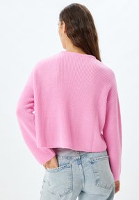 Blandning av bomullssweater i knallrosa, ribbad textur, kort design med långa ärmar, buren över ljusblå högmidjade jeans.