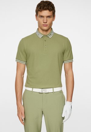 Ljus olivgrön polo t-shirt med krage och logotyp i vit rand, kortärmad, tre-knapps knäppning, i kombination med matchande byxor och ett vitt bälte.