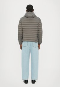 Jachetă puf gri cu cusături orizontale și glugă atașată, purtată cu pantaloni din denim bleu deschis, cu croială largă. Botine negre completează ținuta.