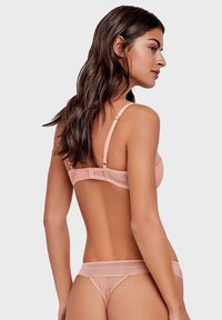 Ensemble de lingerie rose clair comprenant un soutien-gorge en mesh transparent avec des bretelles réglables et un string assorti en mesh transparent, orné de motifs à pois.
