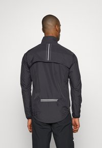 Schwarze leichte Jacke mit hohem Kragen, reflektierenden Akzenten und einer Reißverschlusstasche auf der Rückseite. Mit einem gebogenen Saum und elastischen Bündchen.