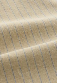 Tissu beige avec fines rayures verticales bleues, matériau tissé texturé, présenté avec de doux plis et des ombres légères.