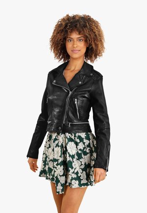 Black leather biker jacket with asymmetrical zip, two front pockets, and a fitted design, paired with a green floral skirt.