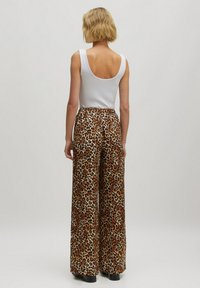 Witte mouwloze top gecombineerd met wijde leopardprint broek in bruin en oranje tinten, met een zachte, gestructureerde stof en elastische tailleband.
