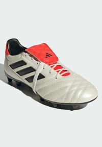 Botín de fútbol de cuero blanco con acentos rojos y rayas negras. Parte superior texturizada con diseño acolchado, tachuelas negras en la suela para tracción.