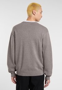 Maglione grigio a maglia con taglio loose, polsini e orlo a costine, e scollatura rotonda. Tessuto grigio morbido con un design semplice.