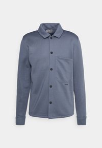 Camisa de algodón azul con botones, cuello, mangas largas, un bolsillo frontal y botones negros. Textura suave y diseño minimalista.