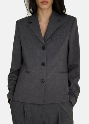 Blazer ajusté gris en tissu texturé, avec un col en pointe, quatre boutons noirs et une poche poitrine.
