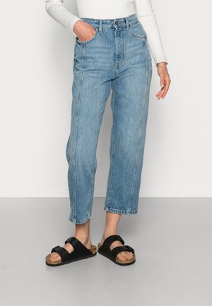 Lichtblauwe high-waisted denim jeans met een rechte pijp en een rafelige zoom, gecombineerd met zwarte sandalen met twee brede banden.