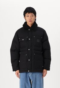 Schwarze gepolsterte Jacke mit einem Fellkragen, mehreren Fronttaschen mit Druckknöpfen und einem eleganten, strukturierten Design.