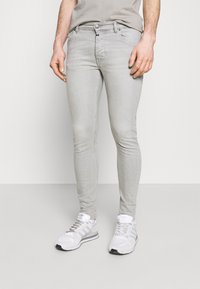 Jeans ajustados de un gris claro hechos de denim, con un diseño clásico de cinco bolsillos y cremallera en la bragueta. Combinados con zapatillas deportivas blancas.