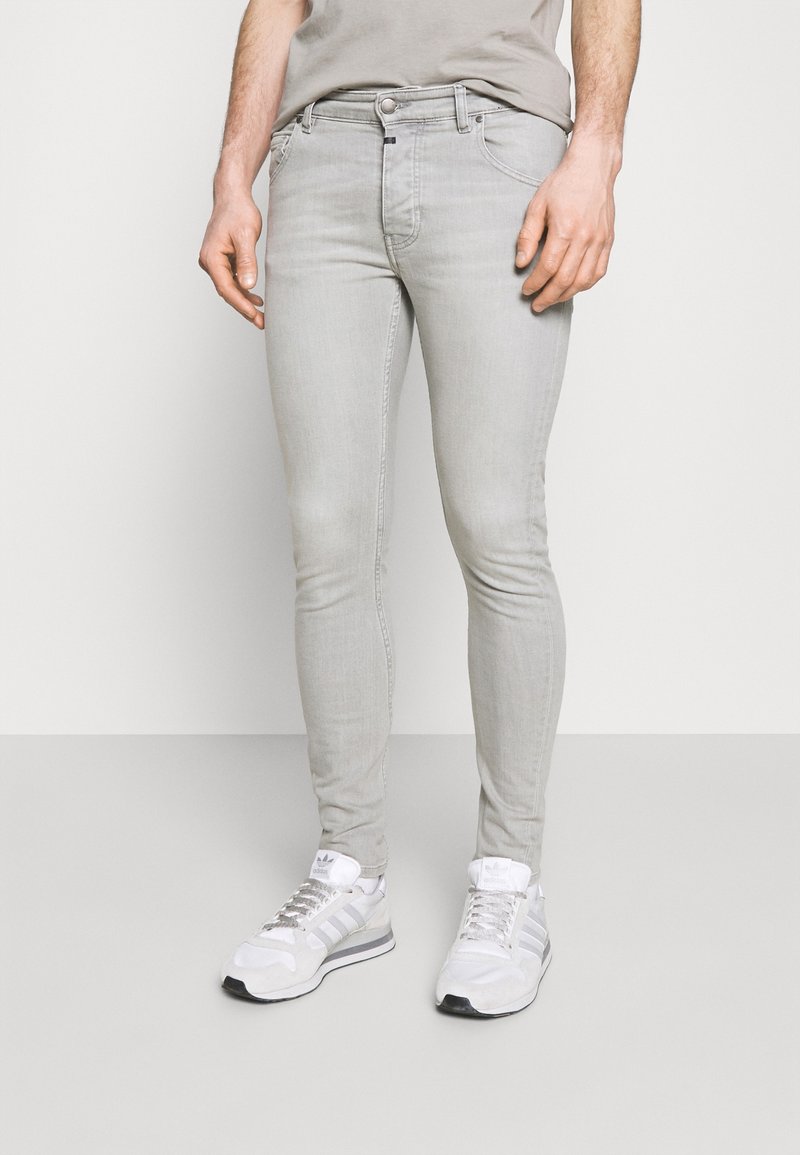 Jeans ajustados de un gris claro hechos de denim, con un diseño clásico de cinco bolsillos y cremallera en la bragueta. Combinados con zapatillas deportivas blancas.