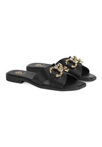 Sandales à glissière en cuir noir avec une semelle plate, dotées de deux brides croisées, d'un bout ouvert et d'une boucle décorative en or et cristal.