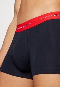 Tengerészkék pamut boxeralsó piros elasztikus derékpánttal, amelyen fehér "TOMMY HILFIGER" logó található. Simább textúra, testhezálló forma.